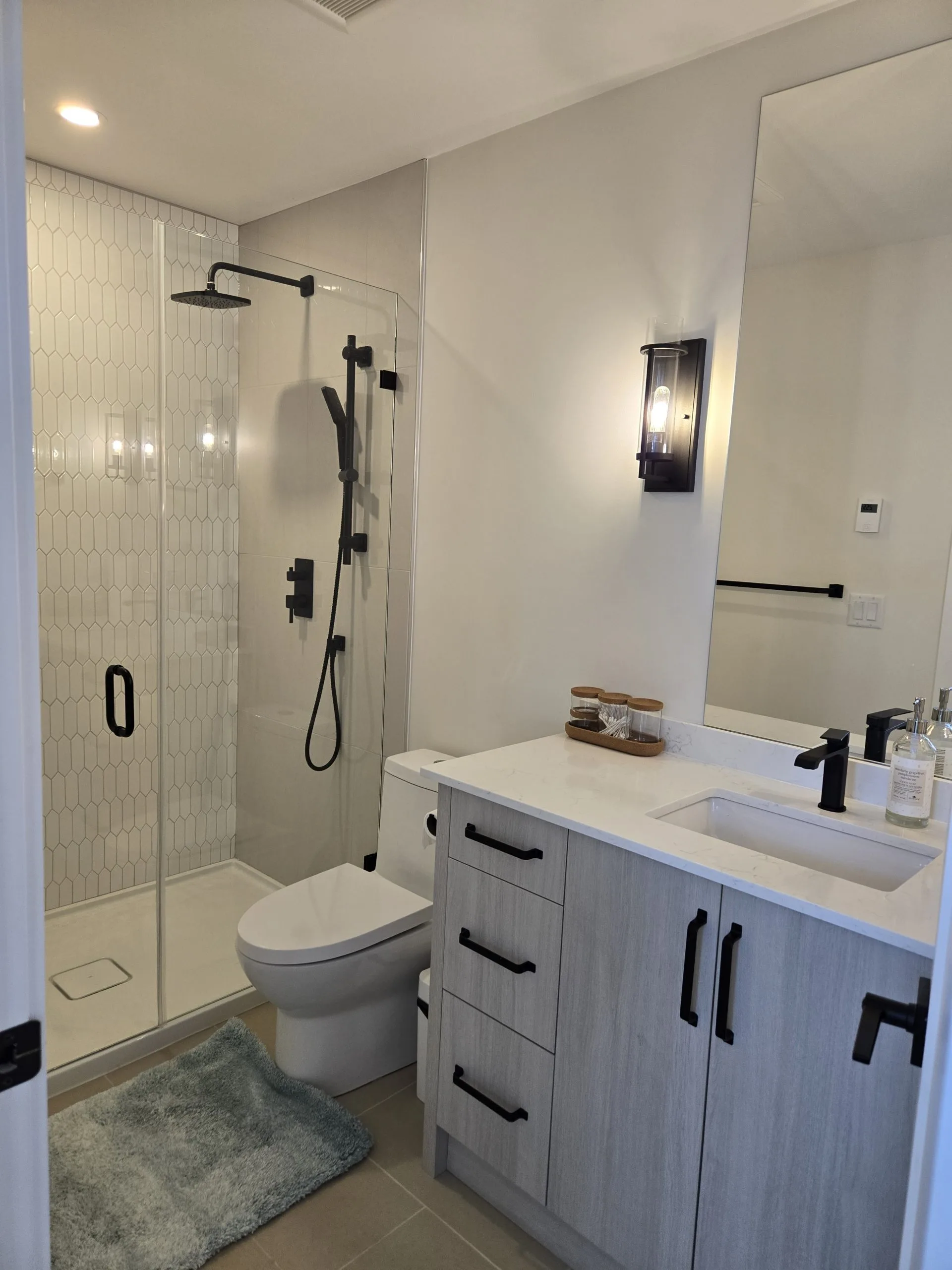 A modern bathroom features a shower, toilet, and sleek vanity with lighting