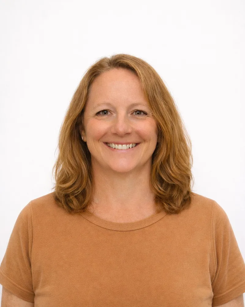 A smiling woman with shoulder-length hair stands against a plain background