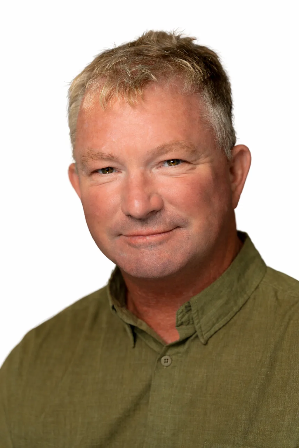 A middle-aged man with short, light hair smiles warmly, wearing a green collared shirt