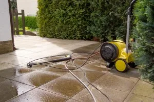 A yellow wet vacuum sits next to a puddled patio, with hoses draped