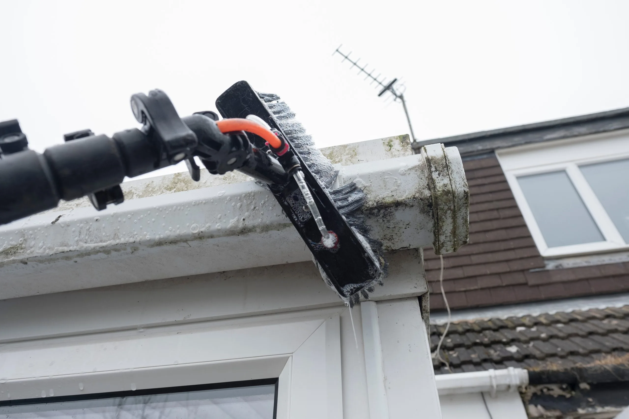 A brush attached to a pole cleans grime from a building's gutter
